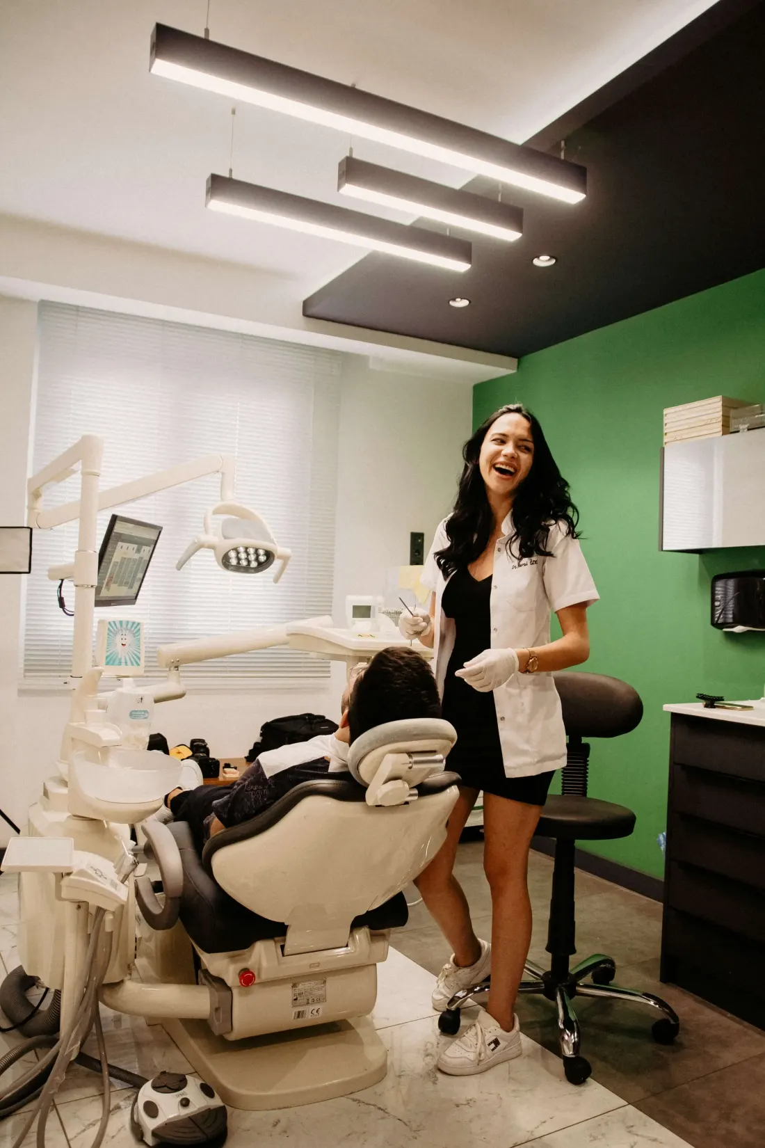 A smiling dentist in a white coat laughing with a patient in a modern treatment room